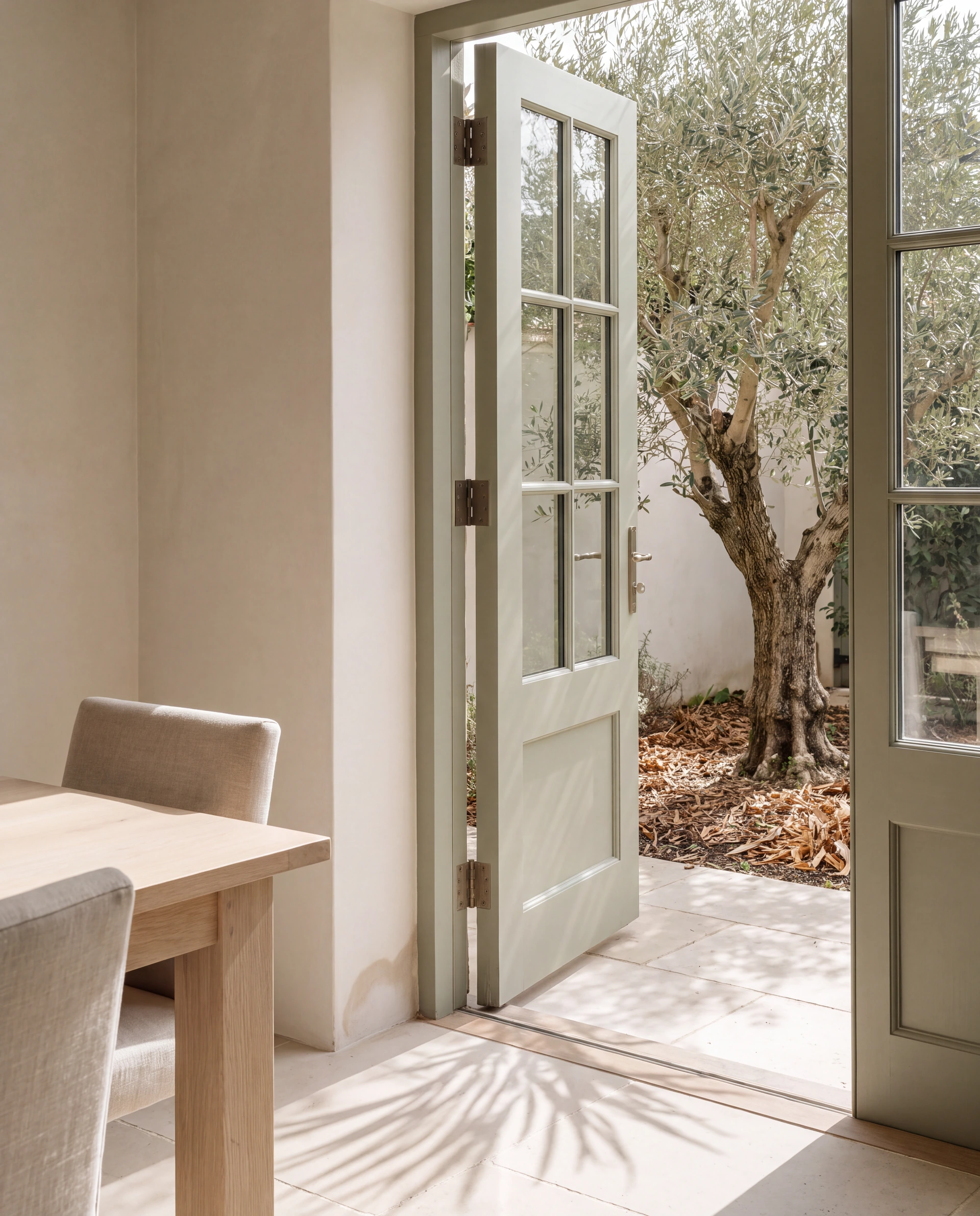 Illustrative scene of an ivory dining room opening through sage doors onto an olive-tree courtyard.